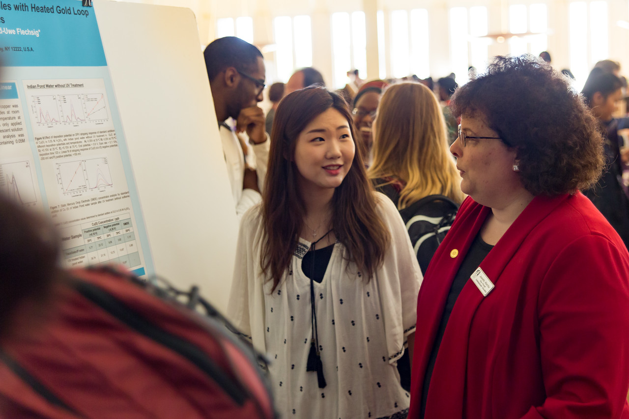 A student displays a research poster with Dean Jeanette Altarriba 