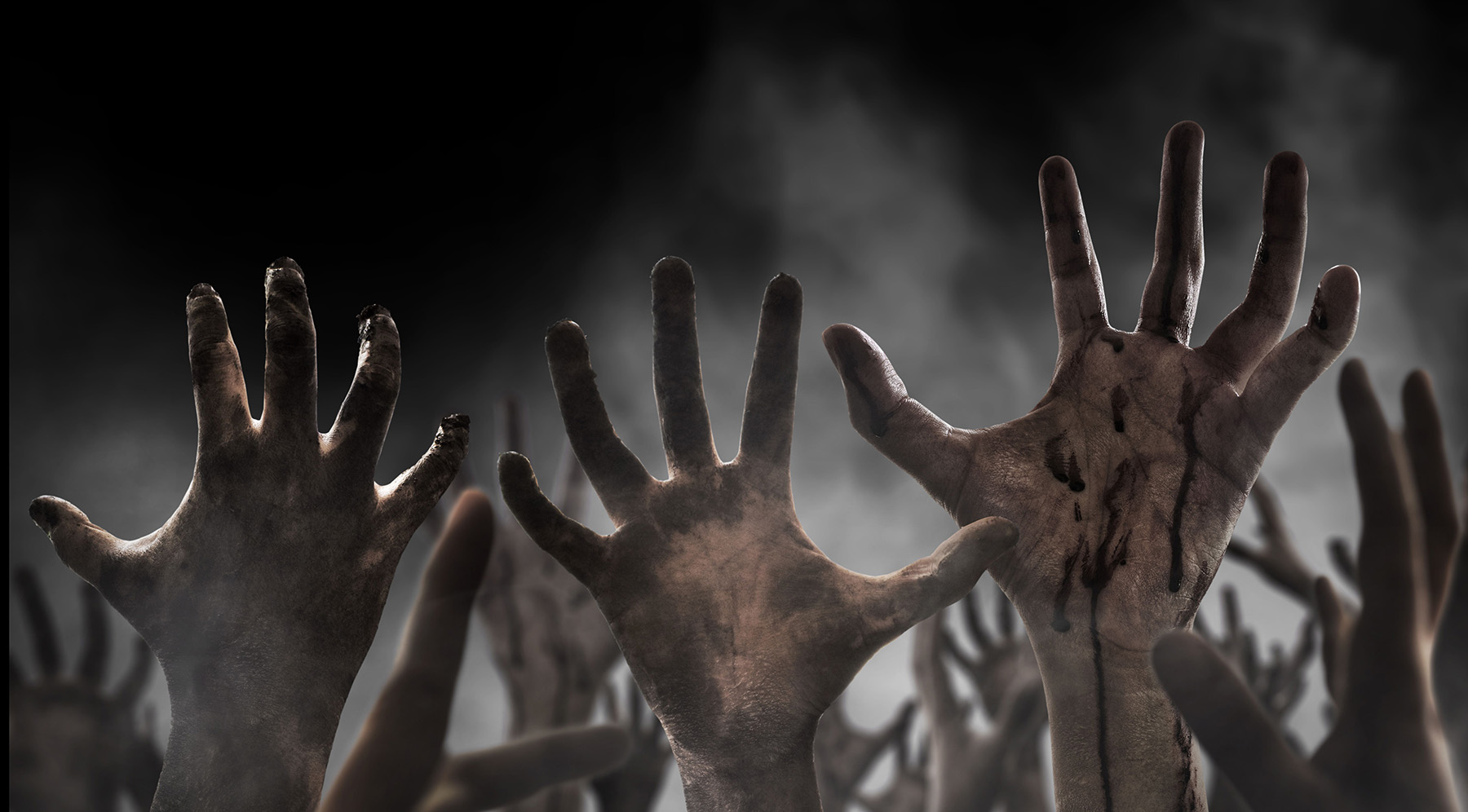 Many scary zombie hands reaching up against a grey, smokey background