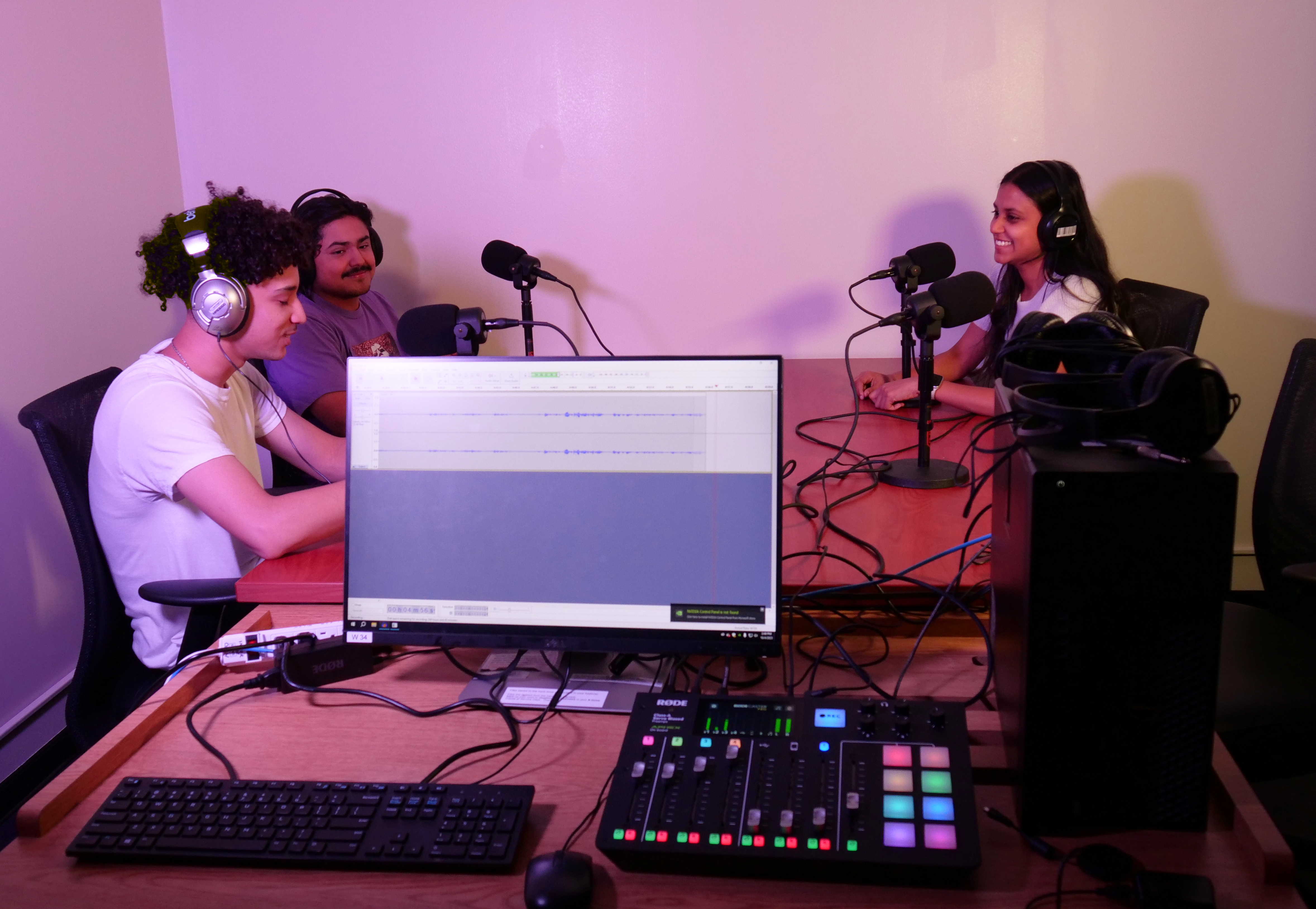 Three people at a table with microphones talking, recording a podcast on a computer