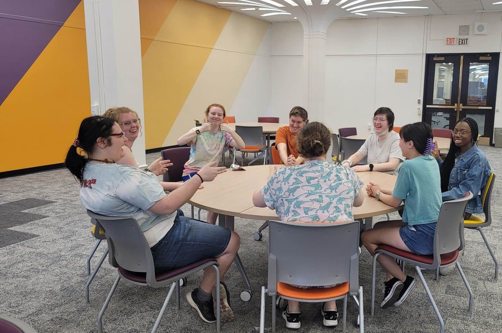 Students laughing and smiling around a circular table in the Minerva room.