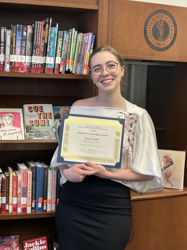 Clancey Staldine poses in front of the Popular Books Collection with her award