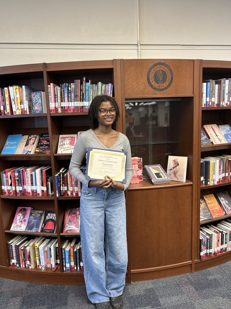 Wania Hermanstyne poses in front of the Popular Books Collection holding an award