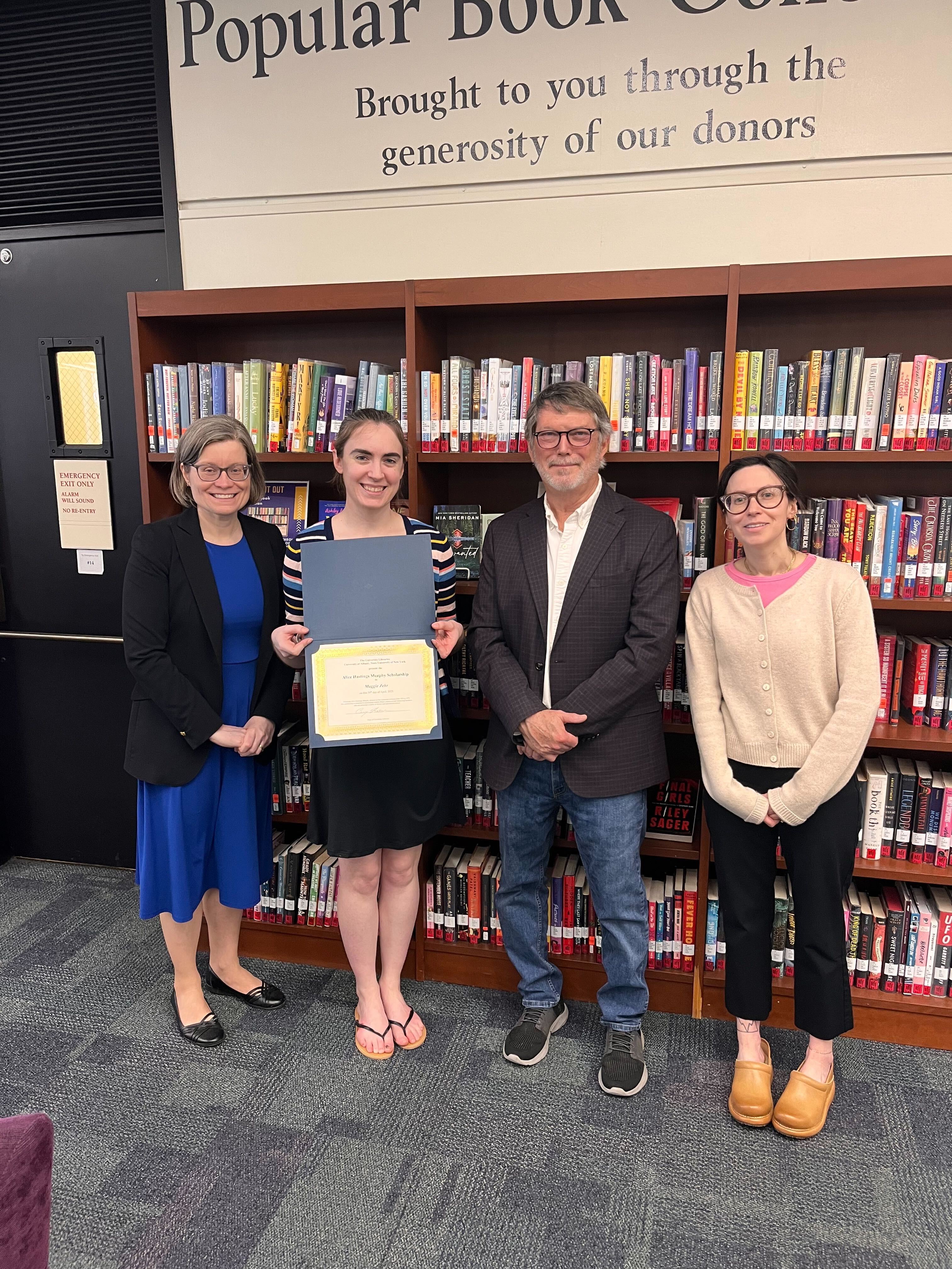 Maggie Zehr poses with Jodi Boyle, Carey Hatch, and Melissa McMullen in front of the Popular Books Collection
