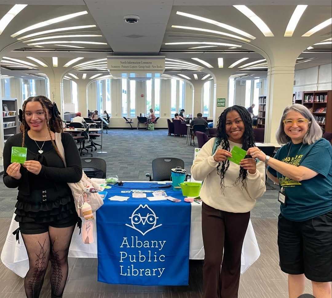 Two students pose with a public library staff member holding library cards