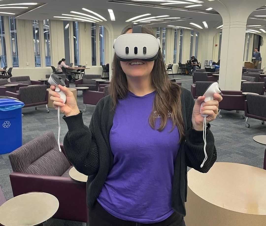 A student in a purple shirt uses a white VR headset, holding two controls.