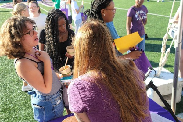 Four students approach a UAlbany Libraries table on the field at Casey Stadium