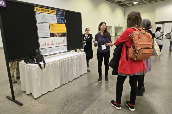 Kelsey O'Brien presenting a poster titled Werewolf on Campus to a group of conference attendees.