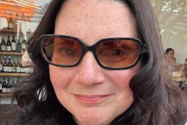 A portrait of a woman, Mary Nyce, wearing sunglasses in front of a cafe