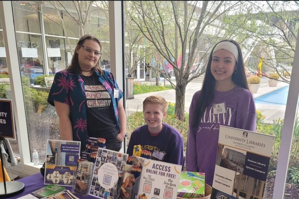 Three students in purple stand behind a UAlbany Libraries table in front of the fountain.