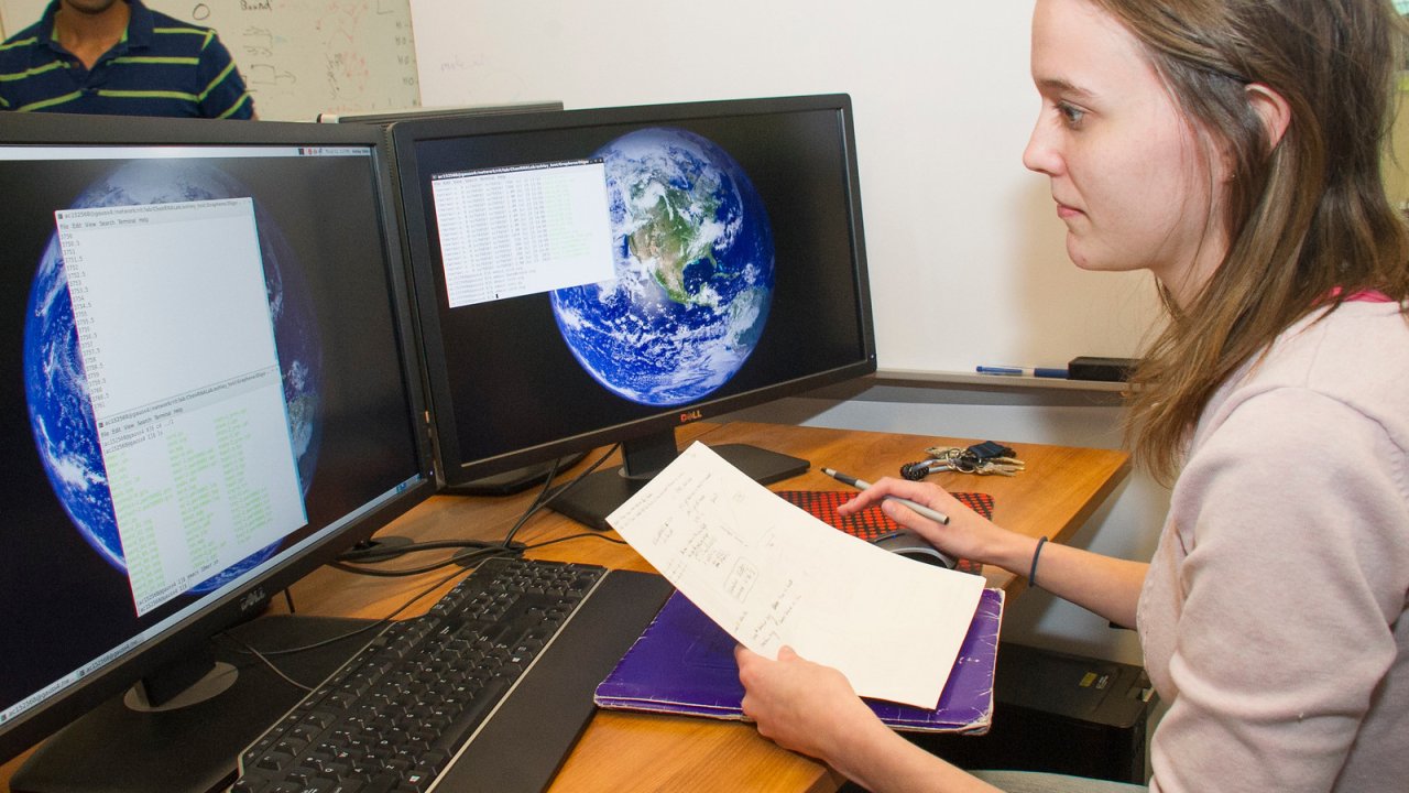 Student intern at computer with code and papers