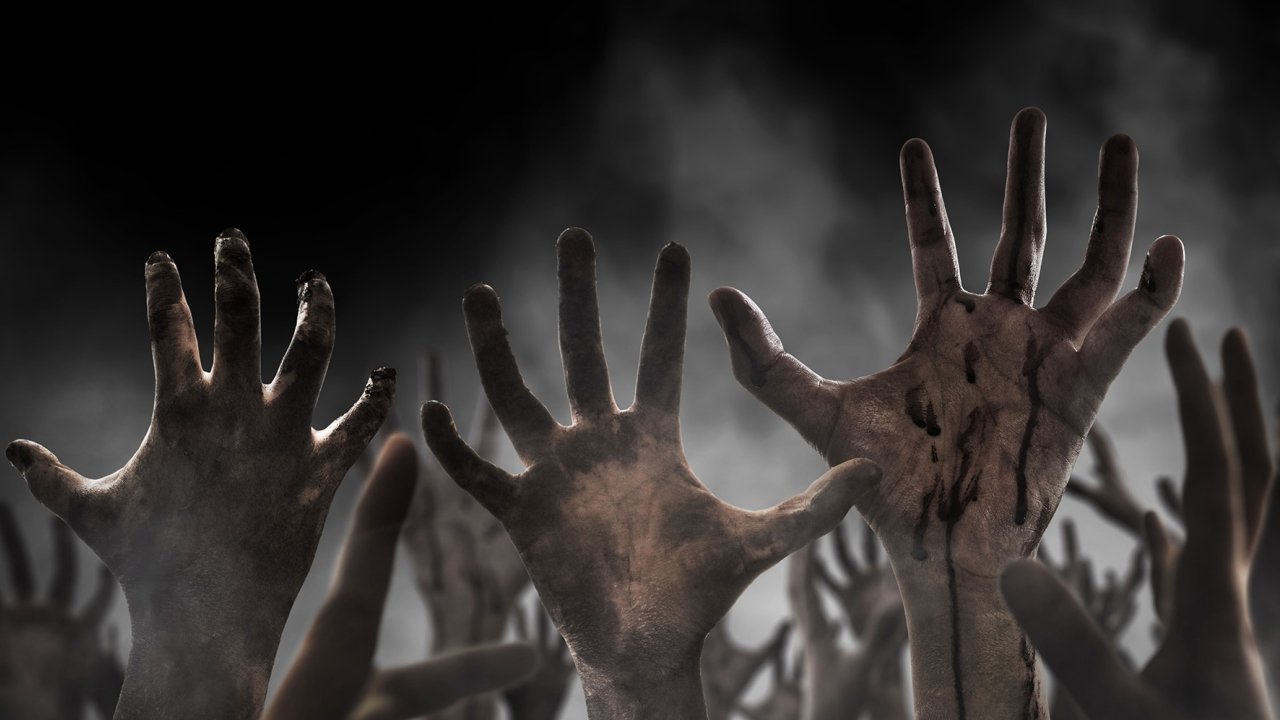 Many scary zombie hands reaching up against a grey, smokey background