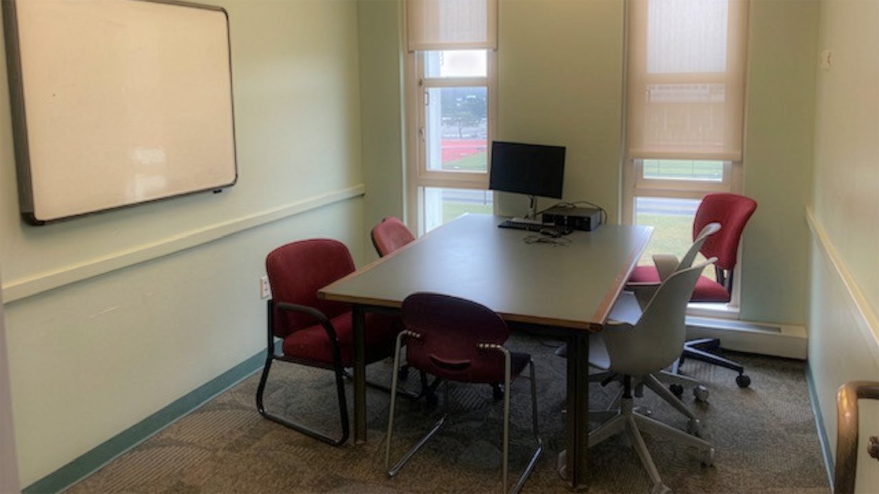 Table with 5 chairs around it sits in an empty room with windows, a whiteboard on one wall and an open door.
