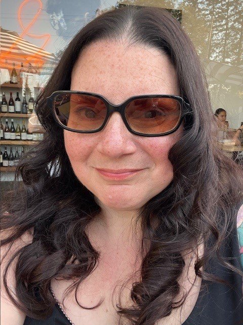 A portrait of a woman, Mary Nyce, wearing sunglasses in front of a cafe