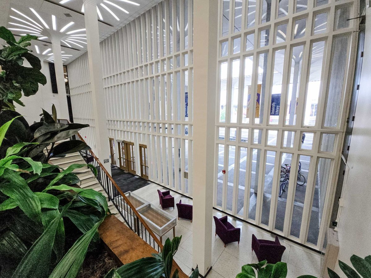 Floor to ceiling windows span two stories of the University Library's main entrance, as shown from the second floor stairs
